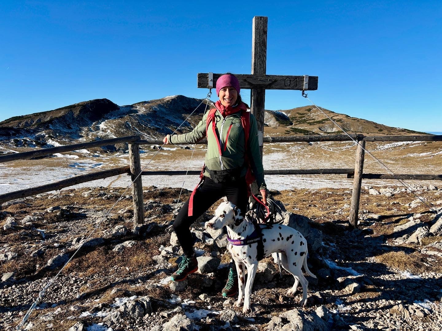 Frau mit Hund bei einem Gipfelkreuz auf Alm