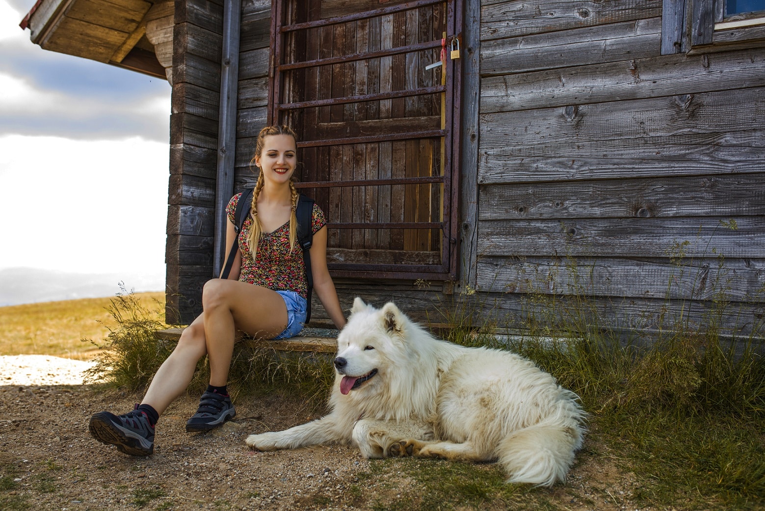 Junge Frau macht mit Hund Rast vor einer Holzhütte.
