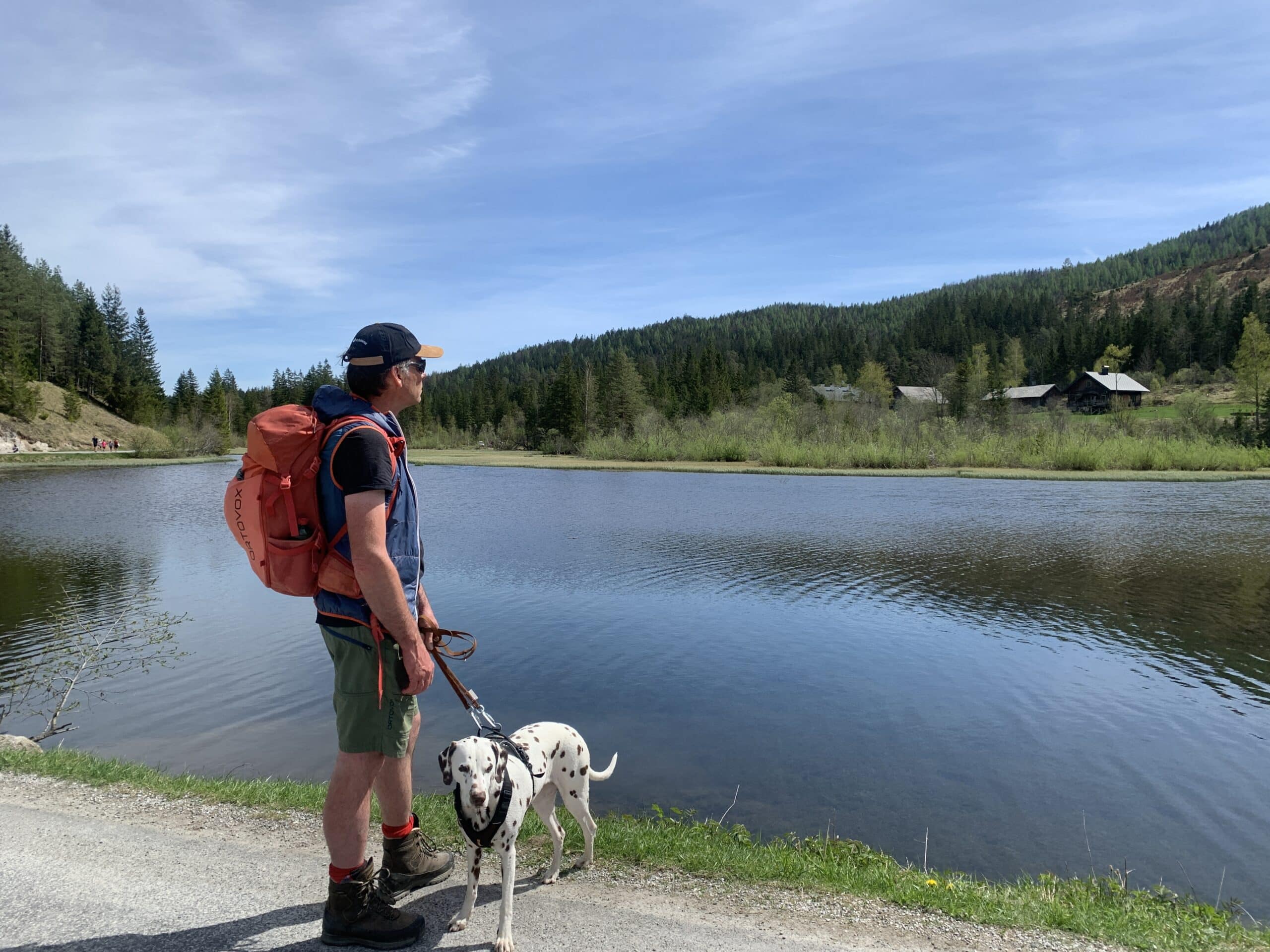 Mann steht mit Hund am Ufer eines Sees