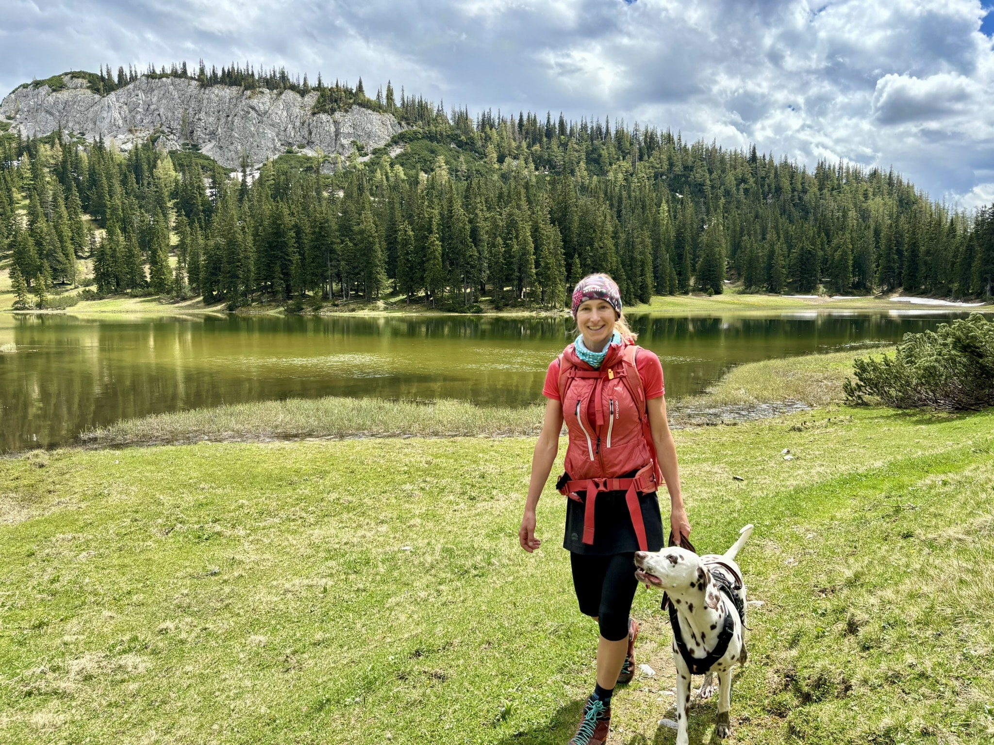 Frau wandert mit Hund an einem Bergsee entlang