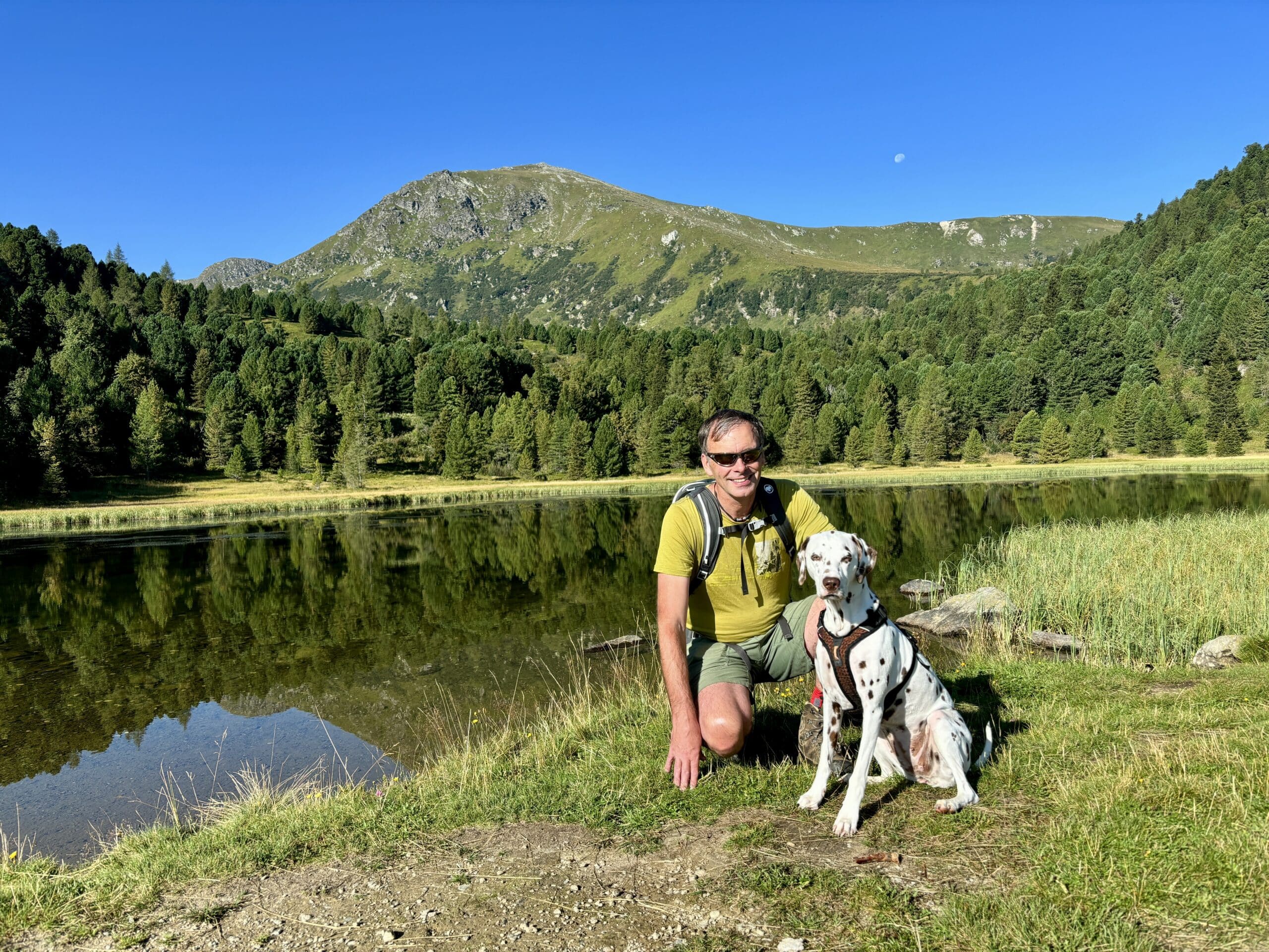 Mann sitzt mit Hund vor einem Bergsee
