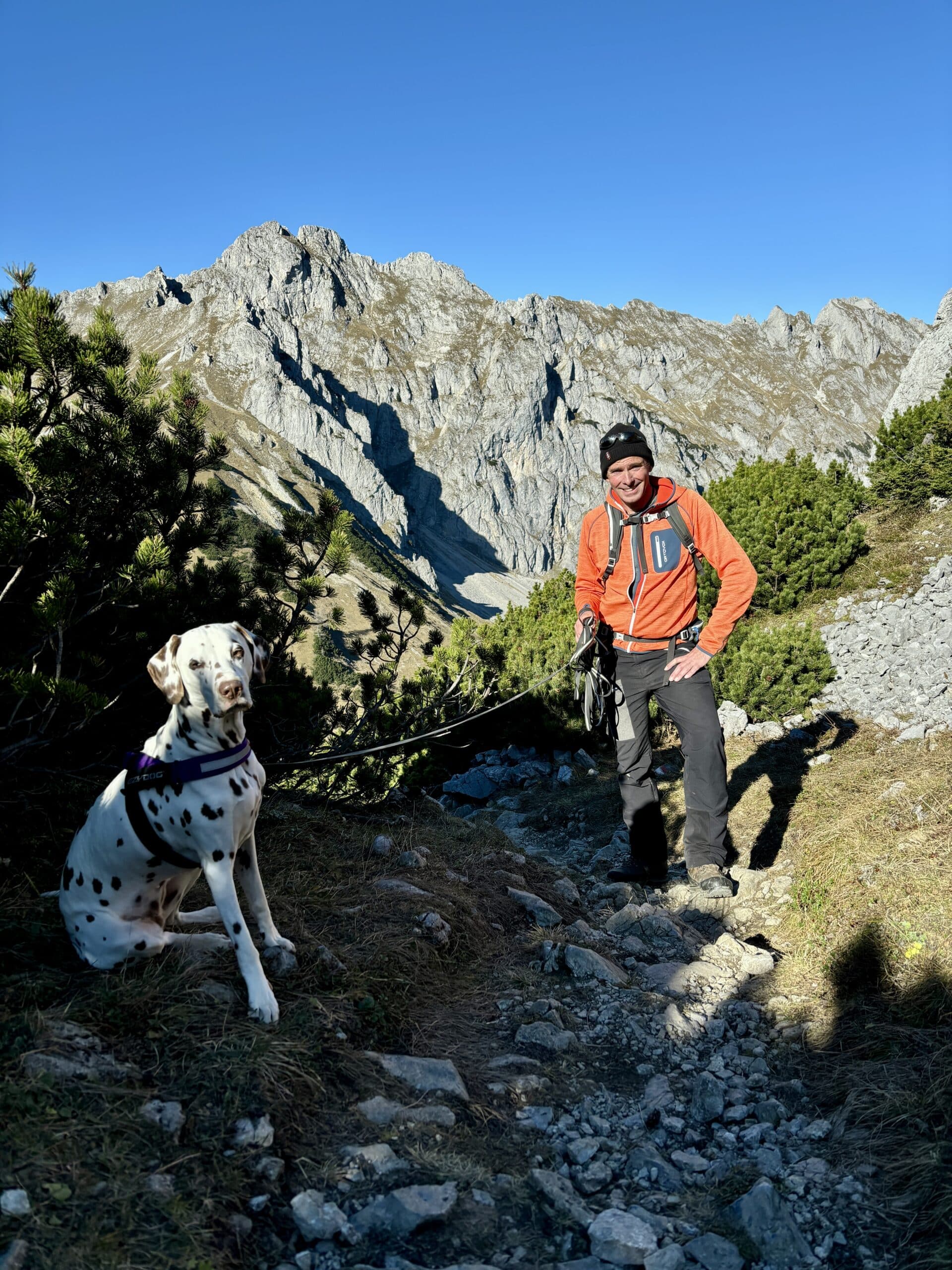 Mann wandert mit Hund auf einem alpinen Weg