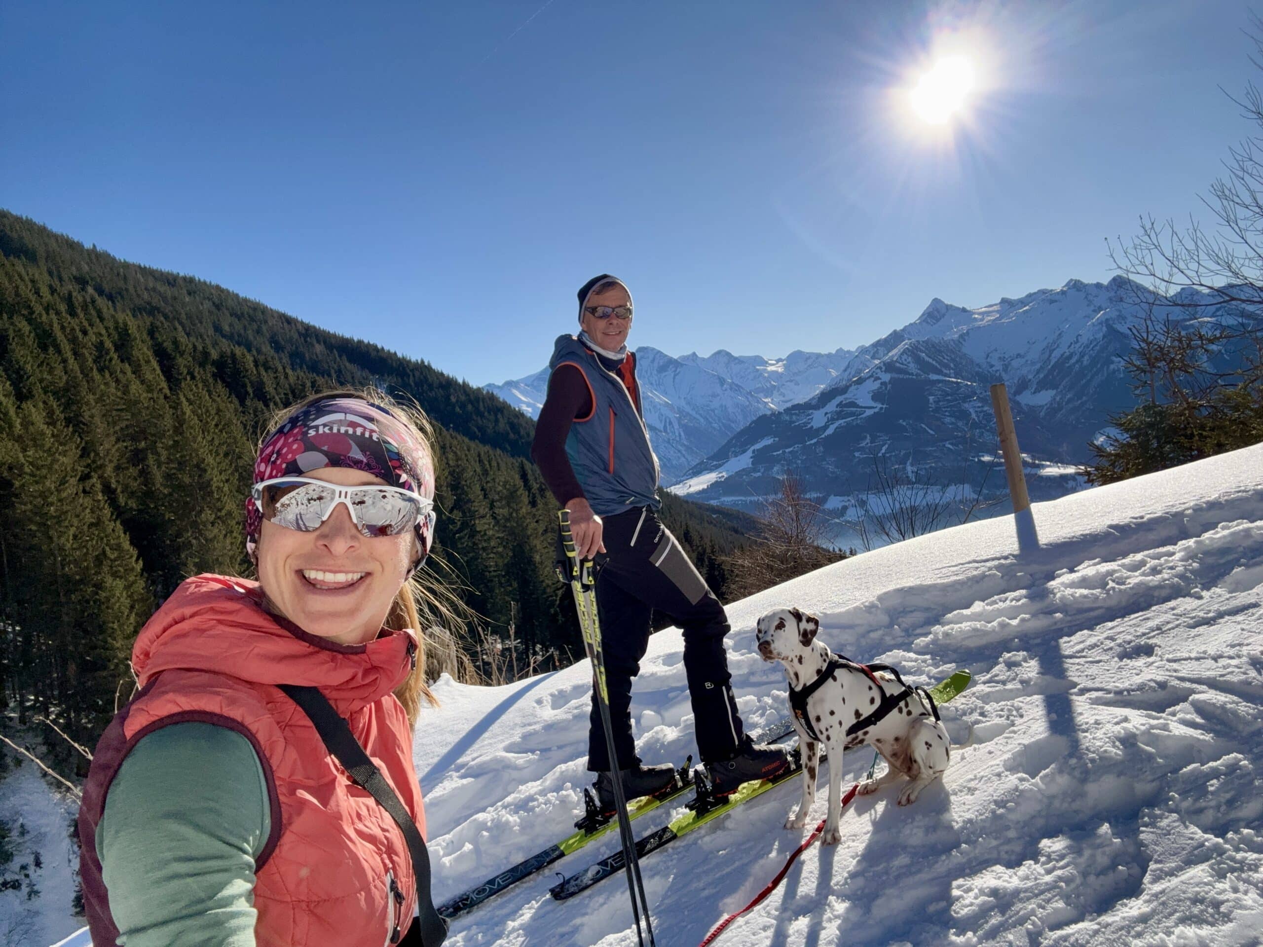 Frau und Mann mit Hund auf Skitour; verschneite Berge; Sonnenschein