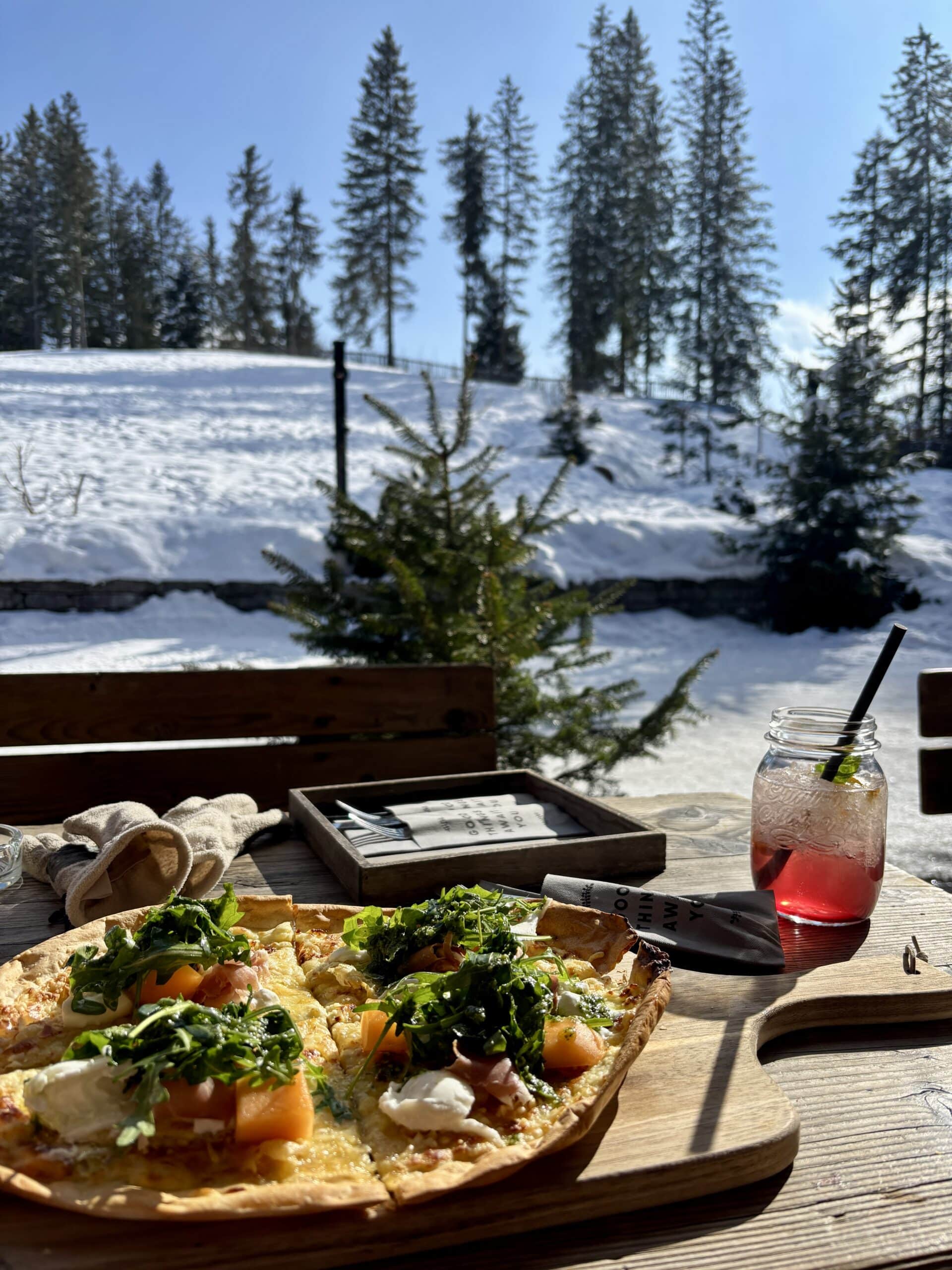 Flammkuchen und Getränk stehen auf Tisch im Außenbereich einen Almhütte.