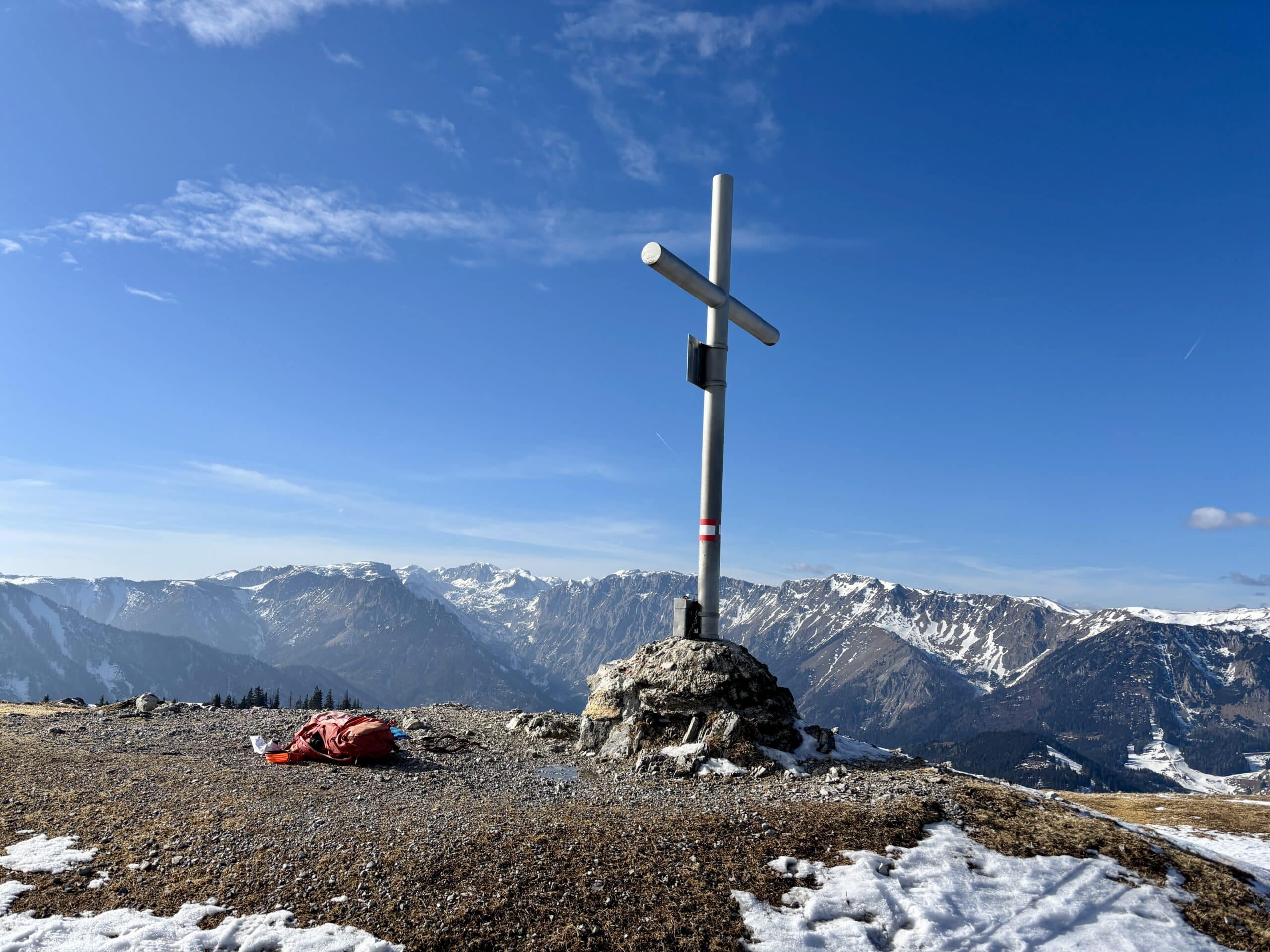 Gipfelkreuz aus Metall, blauer Himmel und Gebirge im Hintergrund