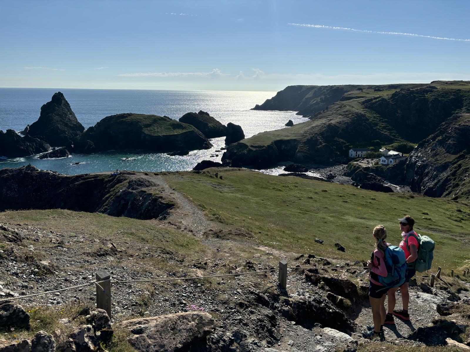 Zwei Frauen stehen mit Wanderkleidung an einem Küstenwanderweg und blicken auf Bucht