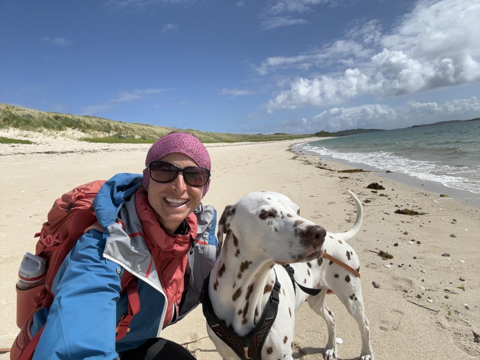 Frau in Wanderkleidung mit Hund an einem weißen Sandstrand