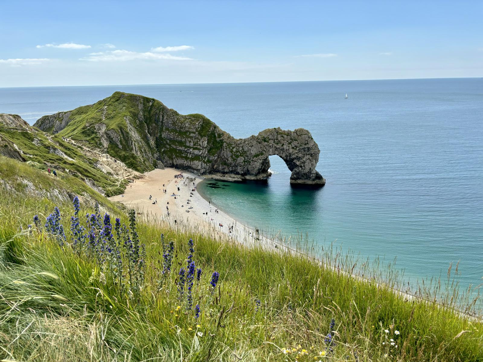 Felsbogen im Meer, weißer Strand; Blumen; Blick auf Steilküste