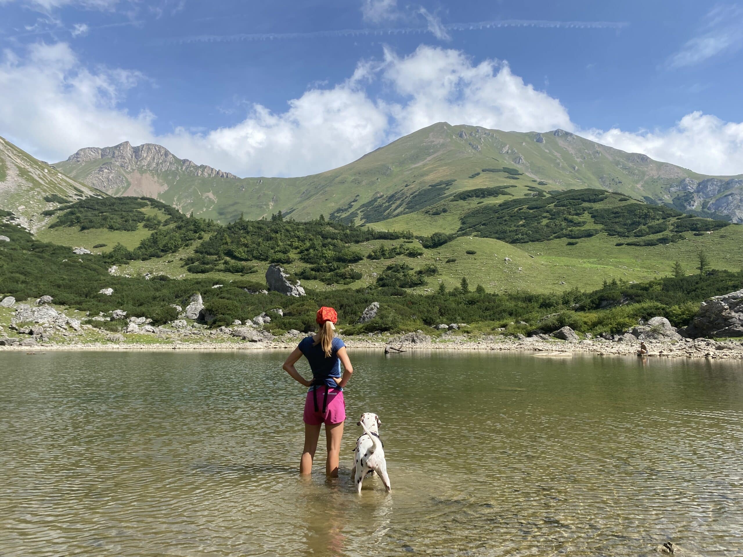 Frau steht mit Hund in einem Bergsee.