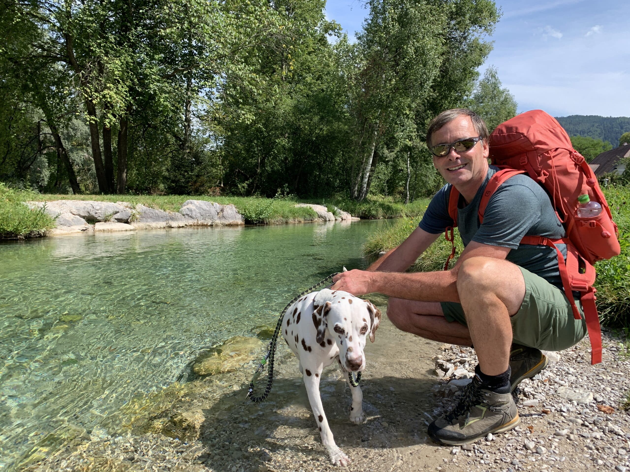 Mann mit Dalmatiner an Schotterbank bei glasklarem Fluss