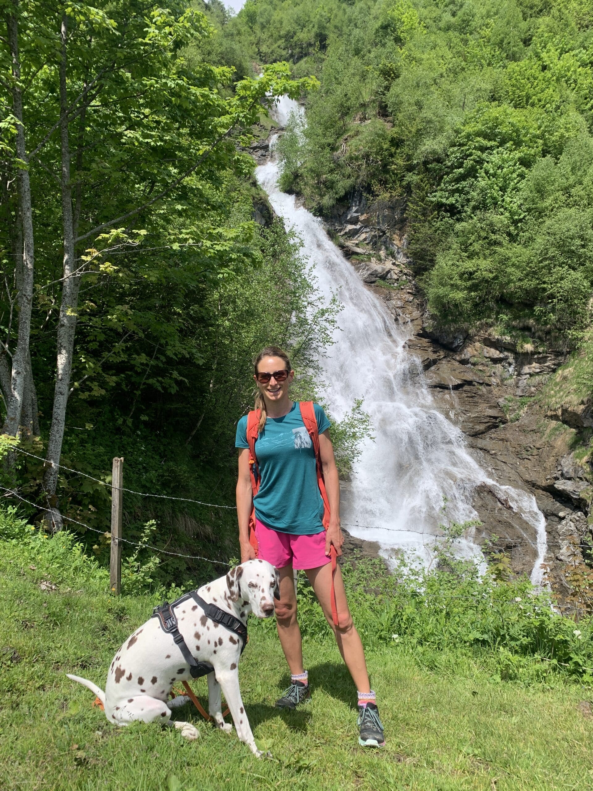 Frau steht in Wanderkleidung mit Hund vor einem Wasserfall