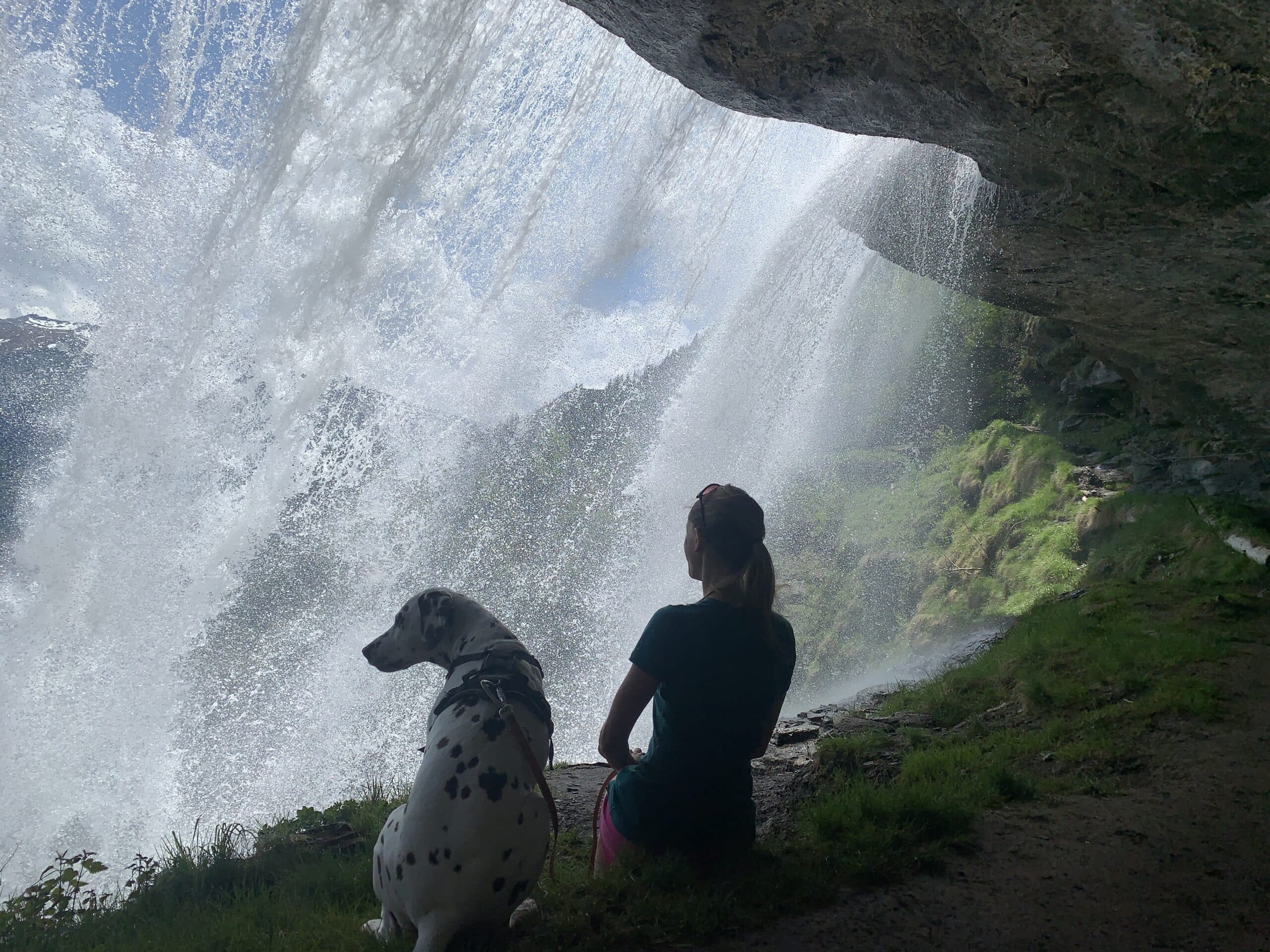 Frau und Hund sitzen hinter einem Wasserfall