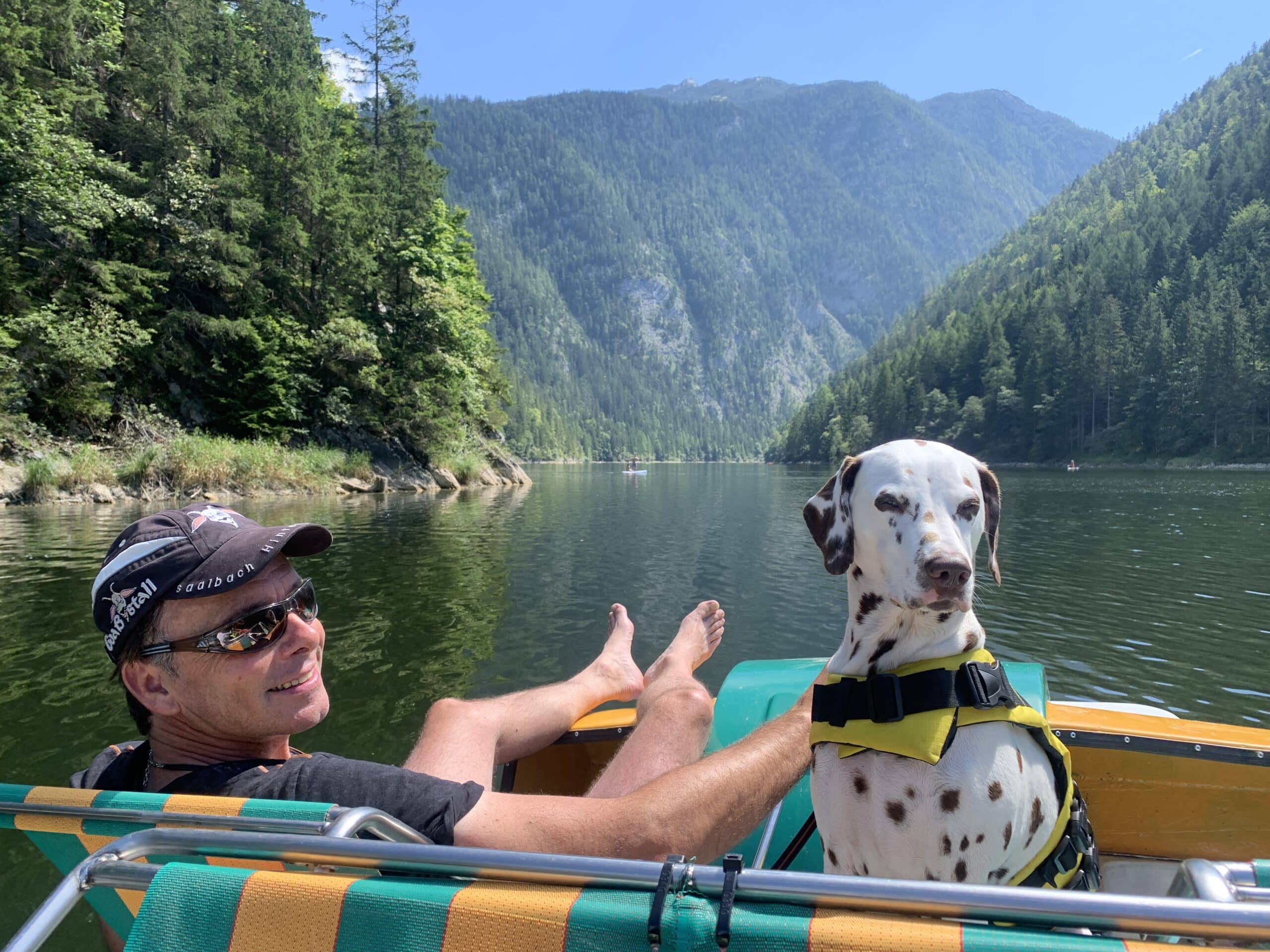 Mann sitzt mit Hund in Tretboot auf einem Bergsee