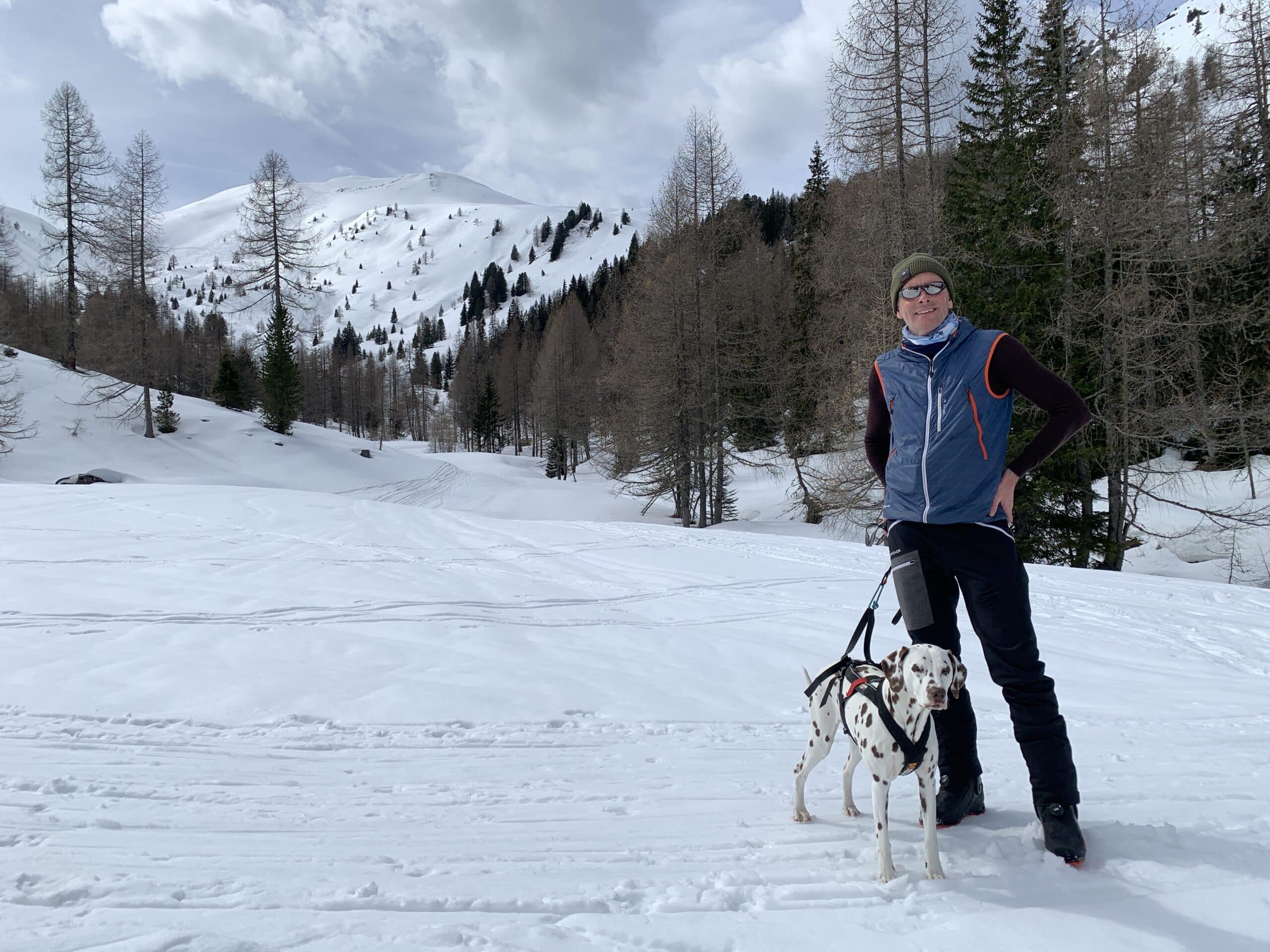 Mann steht mit Hund in Winterlandschaft auf Alm