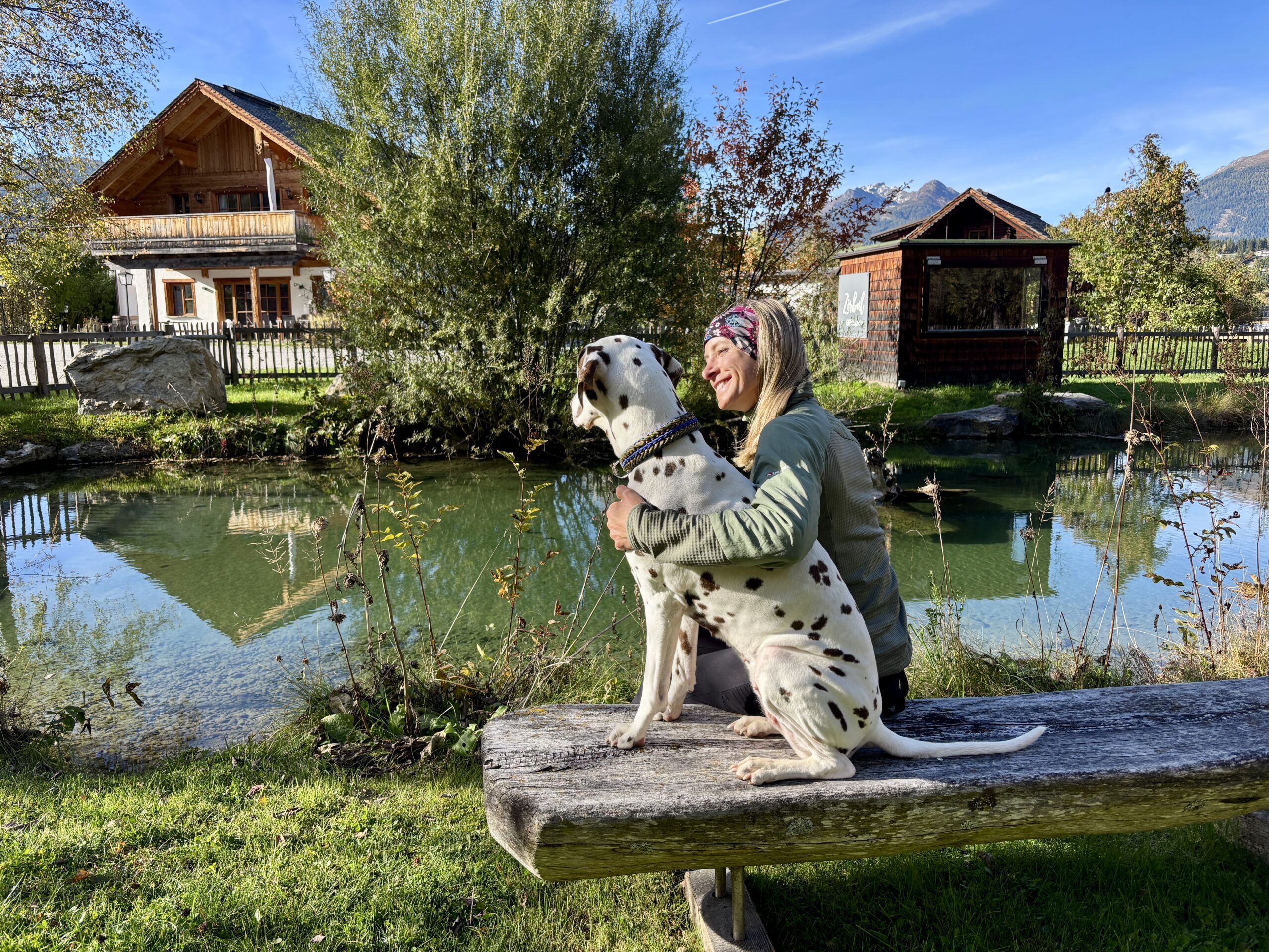 AlpiNest Biotop, Frau sitzt mit Hund auf Holzbank